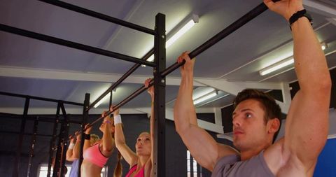 Group performing pull-ups on metal rig in gym demonstrating strength, endurance, teamwork