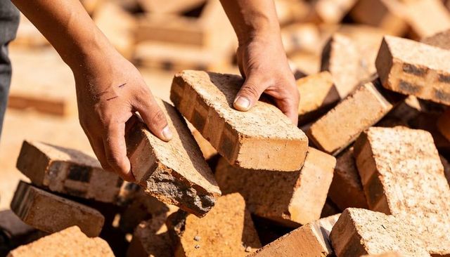 Lifting clay bricks with dusty hands showing scratches and calluses on construction site