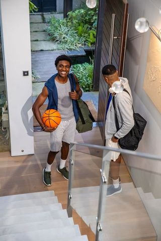 African american friends holding basketball and gym bags at home