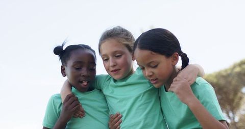 Girls huddling in matching green shirts showing friendship, unity and teamwork outdoors