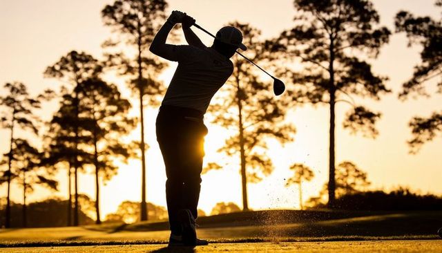 Swinging golfer following through on driving tee at golden hour with turf spray silhouette