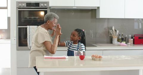 African american grandmother and granddaughter baking together on kitchen island, sharing joyful mom