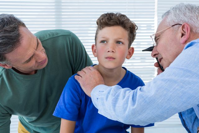Doctor examining young boy's ear while concerned parent watches. Ideal for use in healthcare, pediatric care, medical consultations, family health, and doctor-patient relationship contexts.