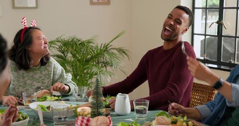 Friends laughing around festive candlelit dining table sharing holiday meal together