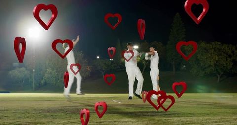Cricket players celebrating under floodlights with floating red hearts at night