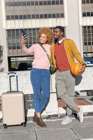 African American Couple Taking Selfie While Traveling with Basketball and Luggage