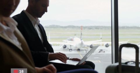 Businessman Typing on Laptop in Airport Departure Lounge