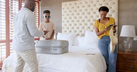 African American family packing for vacation in sunny bedroom with tufted headboard