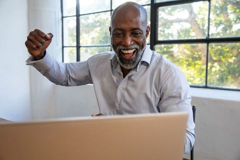 Joyful Mature Individual Celebrates Success with Laptop at Workspace