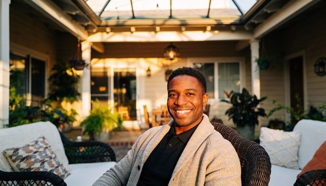 Smiling black man relaxing on sunlit patio in gray cardigan and black polo under skylight