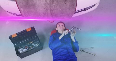 Female mechanic lying under car with tools in automotive garage