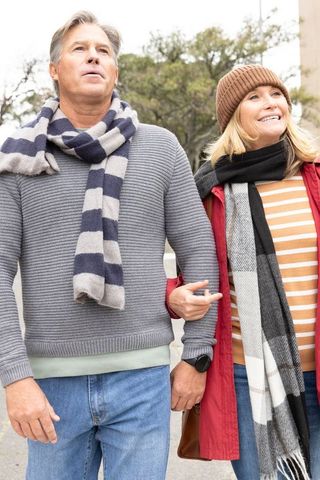 Middle-aged couple walking arm-in-arm on tree-lined city sidewalk wearing scarves
