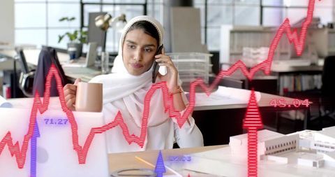 Businesswoman on Phone Analyzing Financial Charts in Modern Office