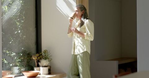 Serene Mature Woman Drinking Coffee in Sunlit Room by Large Window