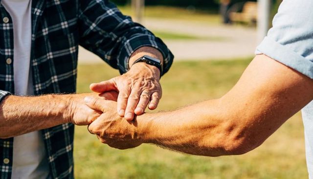 Senior man checking smartwatch while friend guiding wrist outdoors supportive gesture
