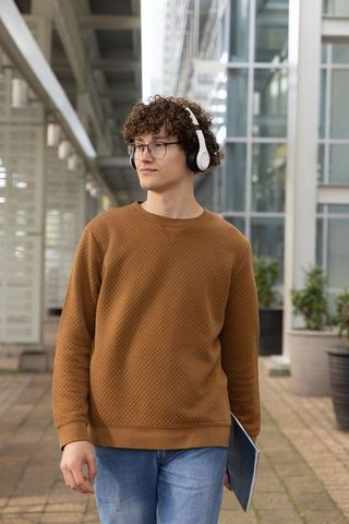 Curly-haired young man walking through urban atrium wearing headphones and holding laptop