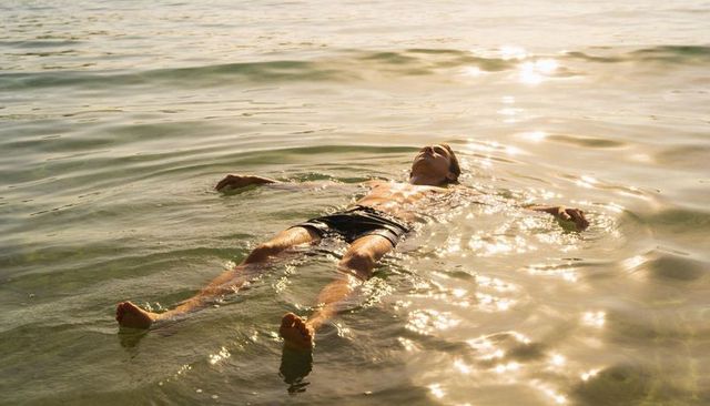 Man floating on calm sunlit sea at golden hour relaxing in shallow water