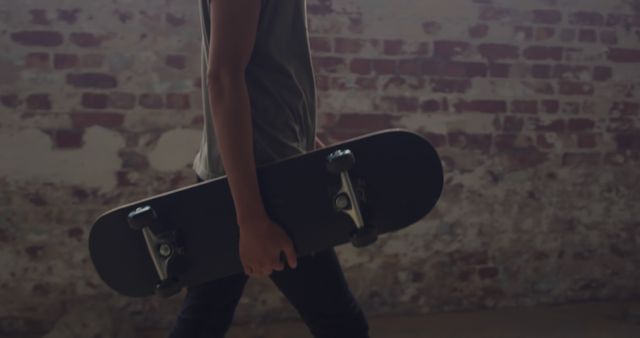 Teen Holding Skateboard Walking Indoor with Brick Wall Background - Download Free Stock Images Pikwizard.com