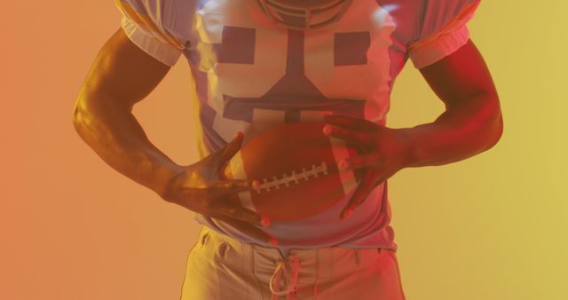 American football player holding football with colorful, gradient lighting creating dynamic and vibrant background. Excellent for sports articles, team promotional materials, and athletic branding.