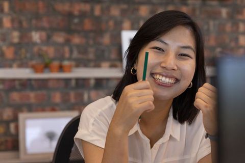 Cheerful young woman in office holding pencil