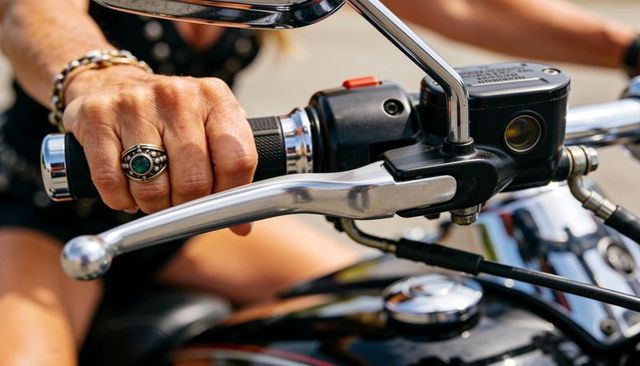 Closeup of hand gripping motorcycle throttle pulling brake lever with green gem ring