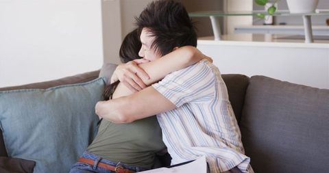 Couple embracing on couch while holding stack of papers, cozy domestic support moment