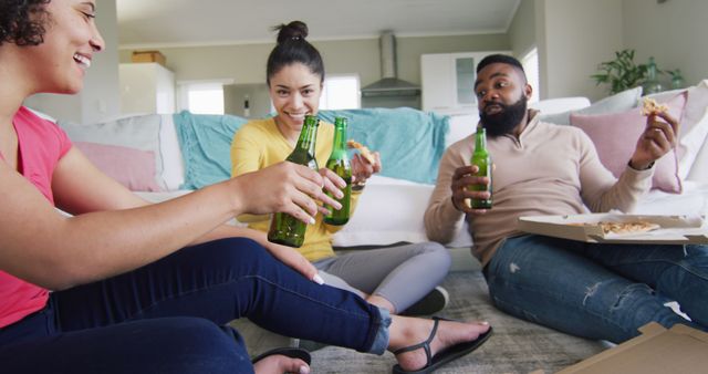 Group of friends sitting on the floor in a living room, eating pizza and drinking beer. Perfect for promoting social gatherings, friendship, food and lifestyle blogs.