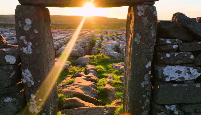 Stone portal framing sunlit limestone pavement with grass tufts at golden hour