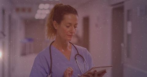 Nurse reviewing digital patient records on tablet in hospital hallway