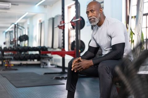 Mature african american man sitting on bench resting between workouts in modern gym