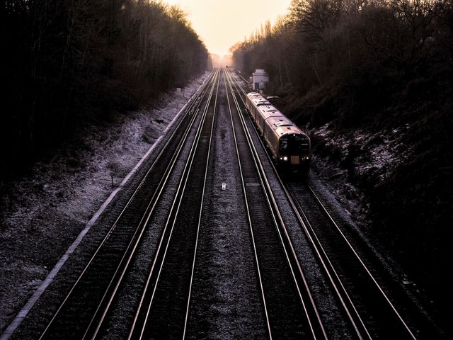 Train traveling along railway tracks during dusk in a winter landscape. Trees and nature surround the rails. Great for content related to transportation, travel, winter journeys, evening sceneries, and the beauty of train travel.