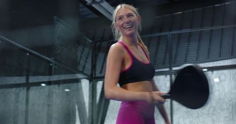 Smiling woman in activewear holding paddle racket on court