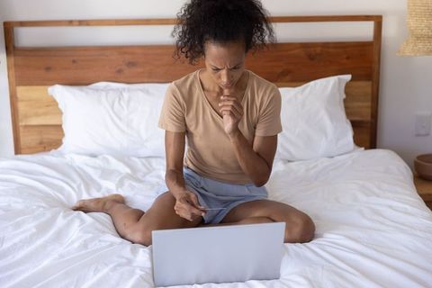 Concerned woman making online payment on laptop while sitting on bed in cozy bedroom