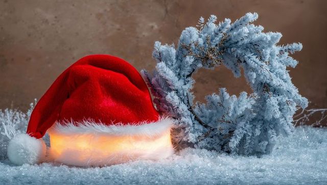Glowing Santa Hat Resting on Snow Beside Frosted Evergreen Wreath