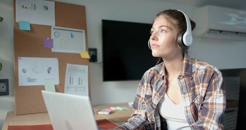 Focused Young Woman with Headphones Working at Cozy Home Office Desk