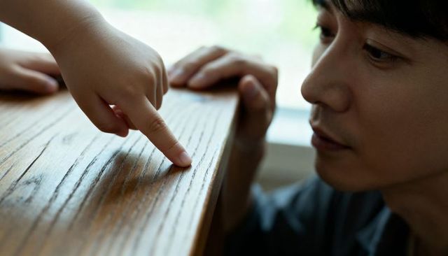 Father guiding toddler finger along wooden table edge closeup nurturing touch and exploration