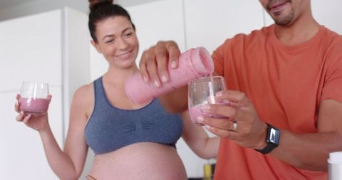 Healthy pregnant couple making smoothies in modern kitchen