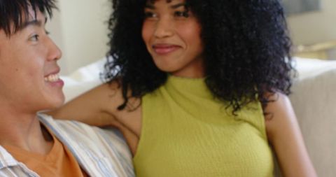 Diverse young couple sharing cozy sofa moment, smiling and connecting in modern living room