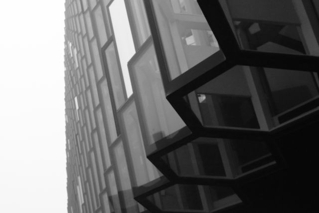 Modern angular glass building showcasing geometric design in black and white. Useful for illustrating concepts of contemporary architecture, urban design, structural engineering, and modern minimalism. Ideal for architectural magazines, urban development articles, and design-oriented websites.
