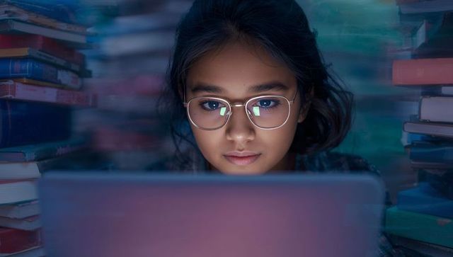 Focused Teenager Using Laptop Surrounded by Books
