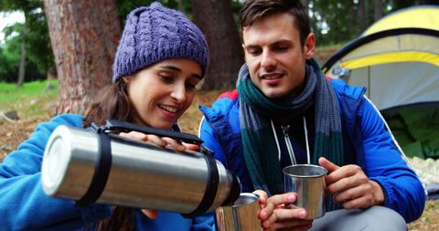 Young couple enjoying cozy beverage moment while camping outdoors