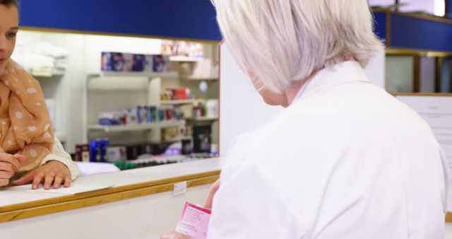 Pharmacist in white coat assisting a customer at pharmacy counter, handling a box of medicine. Suitable for use in health-related articles, pharmacy services promotion, customer service training material, and healthcare marketing content.