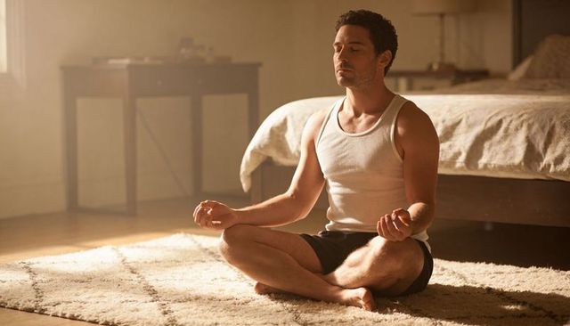 Sunlit morning mindfulness man meditating cross-legged on rug in bedroom