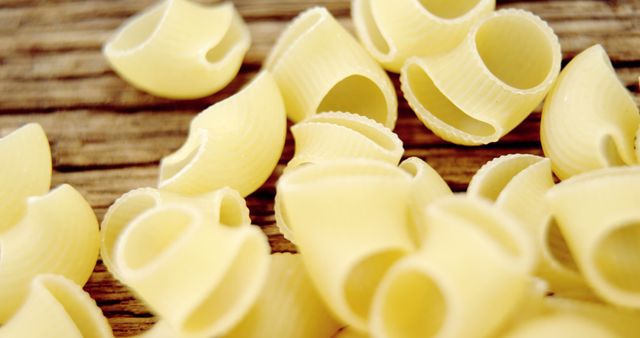 Image shows raw pipe rigate pasta on a wooden surface. Perfect for use in food blogs, culinary websites, and Italian cooking applications. Highlights texture and shape of the pasta.
