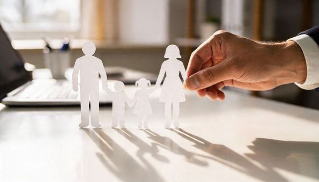 Businessman hand adjusting paper family cutouts representing protection and family insurance