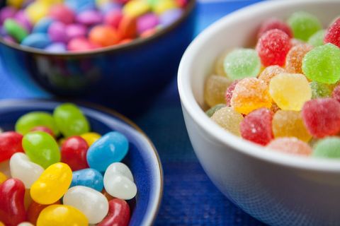 Displaying colorful jellybeans and sugar-coated gumdrops in bowls on blue surface