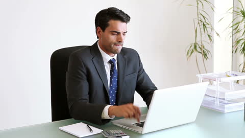 Focused Businessman Working at Office Desk with Laptop and Notepad
