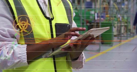 Factory worker using tablet with biohazard overlay in industrial aisle safety inspection