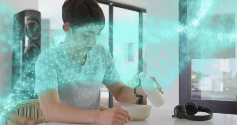 Teenage boy pouring milk into bowl while turquoise digital particles swirl in modern home