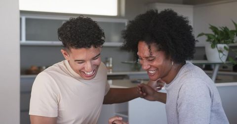 Laughing friends linking arms in modern home kitchen sharing candid moment of joy